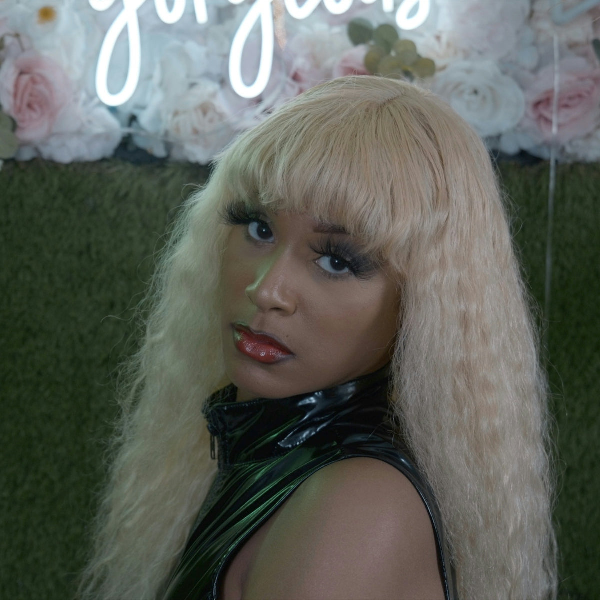 a woman with long blonde hair and a neon sign behind her